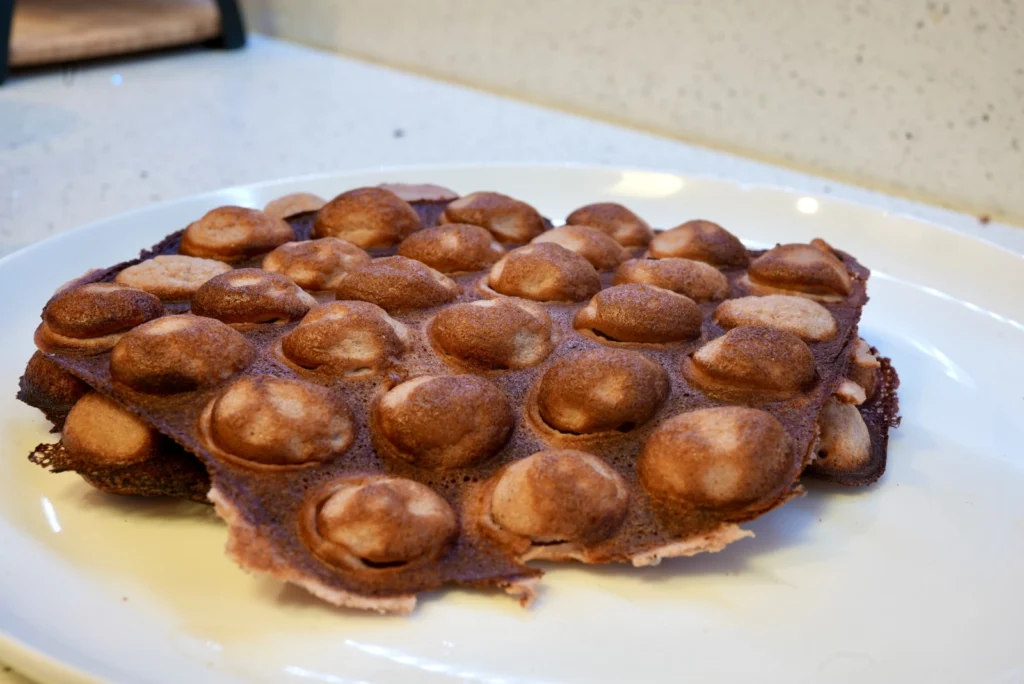 Pink-tinted bubble waffle with caramelized brown crusting on its surface. 