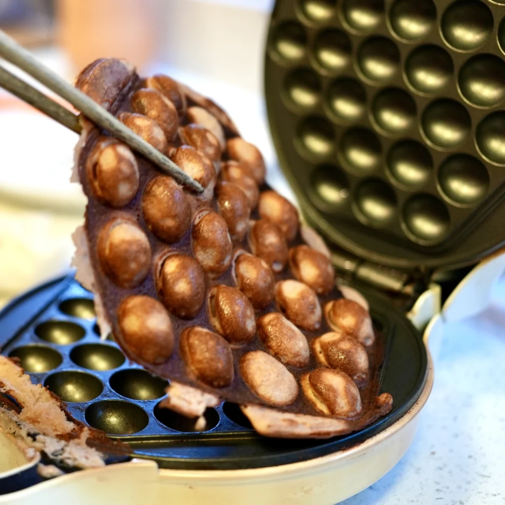 Bubble waffle being lifted from a bubble waffle iron with a pair of chopsticks.